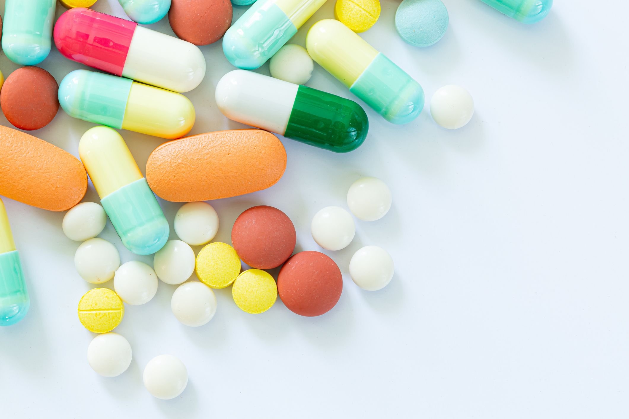 A variety of colorful pills and capsules on a white surface, representing the healthcare and pharmaceutical industry.